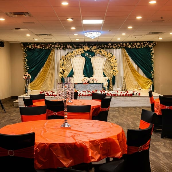 A banquet hall with round tables, red tablecloths, black chairs, and an ornate stage.