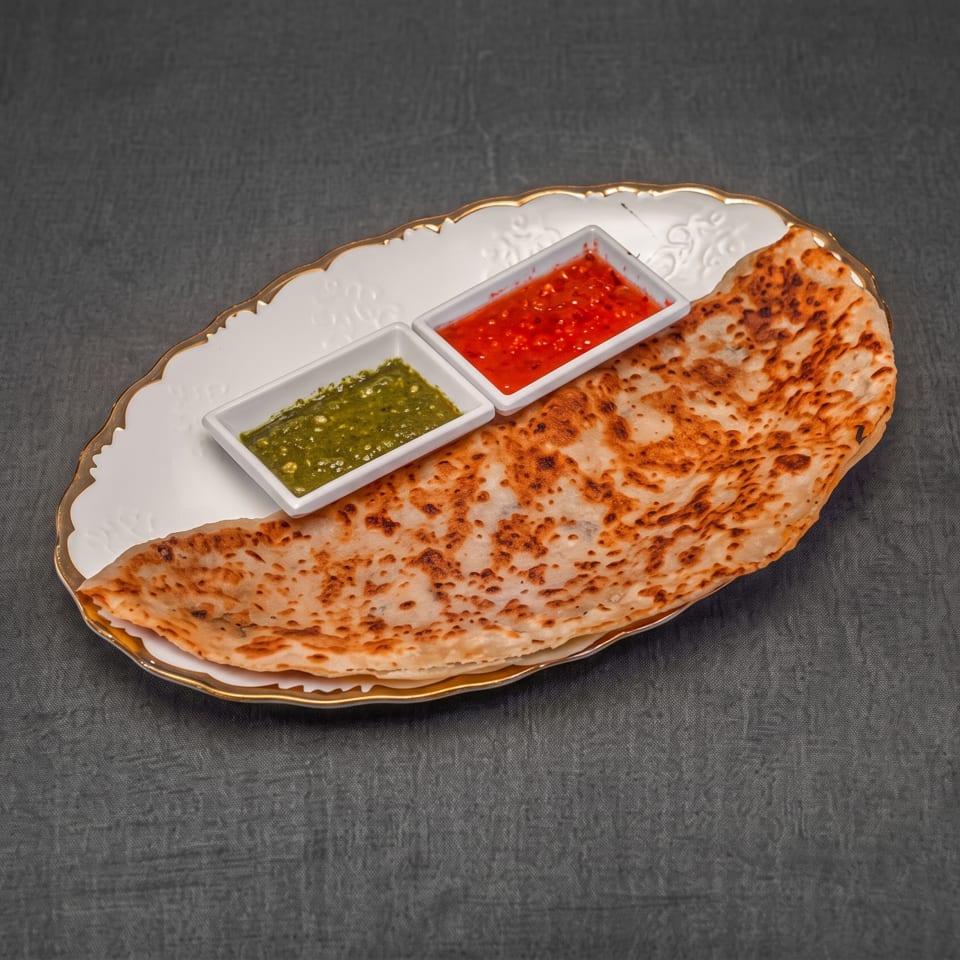 A golden-brown flatbread with two small dishes of green and red sauces on a white plate.