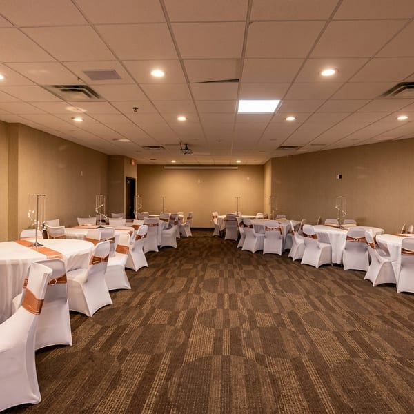 Empty banquet hall with round tables, white tablecloths, and peach runners and chair sashes.