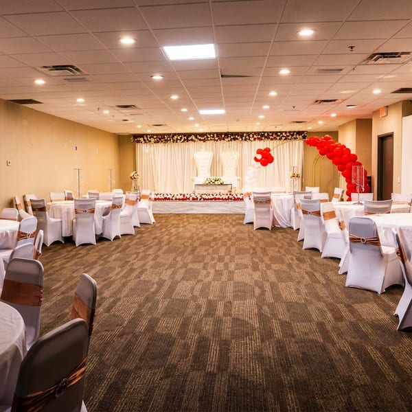 A large banquet hall set up for an event with white tables, chairs, and a decorated stage.