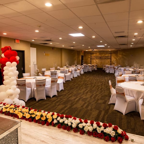 A large banquet hall set up for an event with white tables, chairs, and red and white decorations.